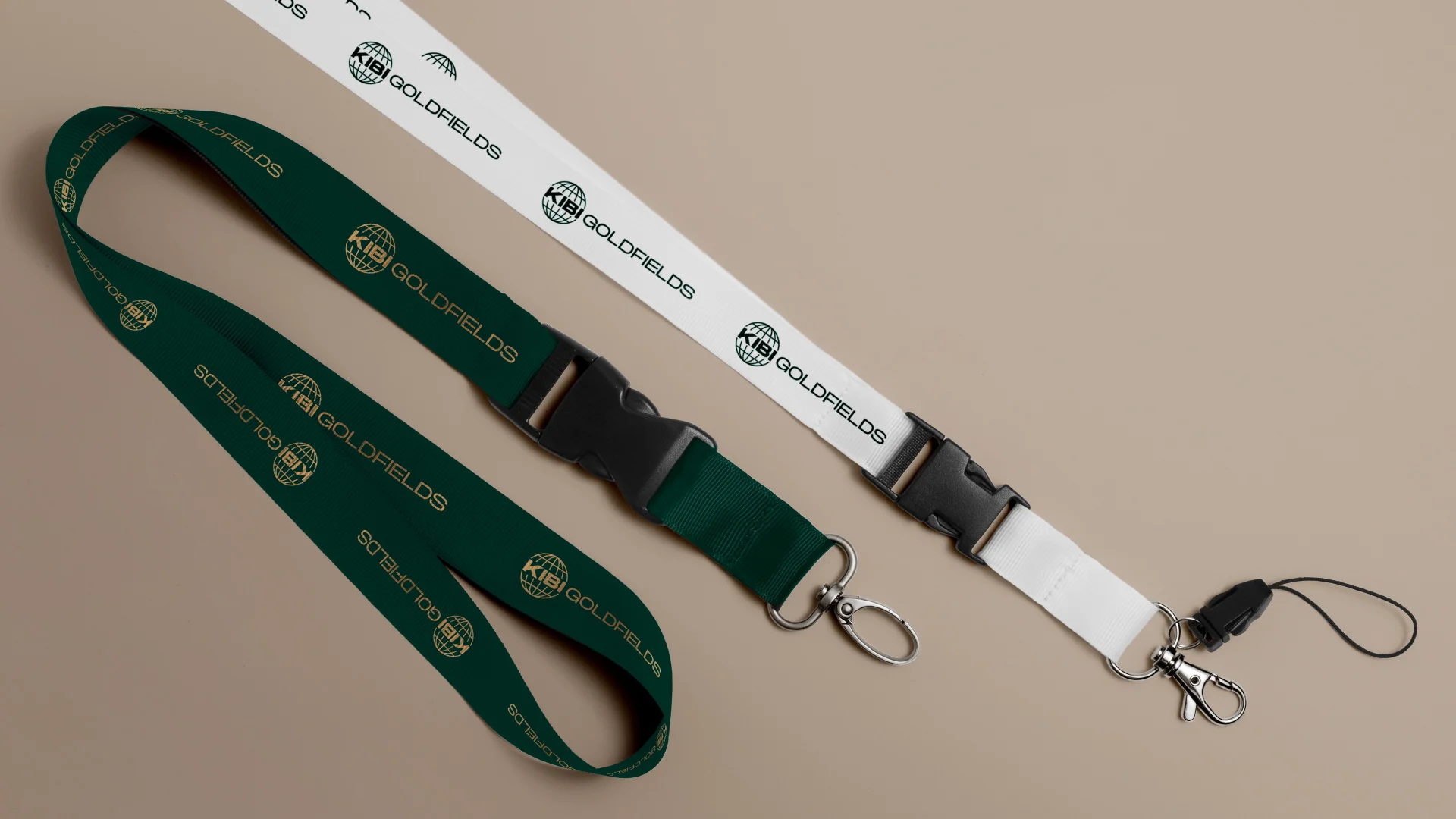 Projeto Kibi Goldfields da Nhdesign: lanyards com o logo da Kibi Goldfields aplicado, um verde com os logos a dourado, e outro branco com os logos a verde escuro.