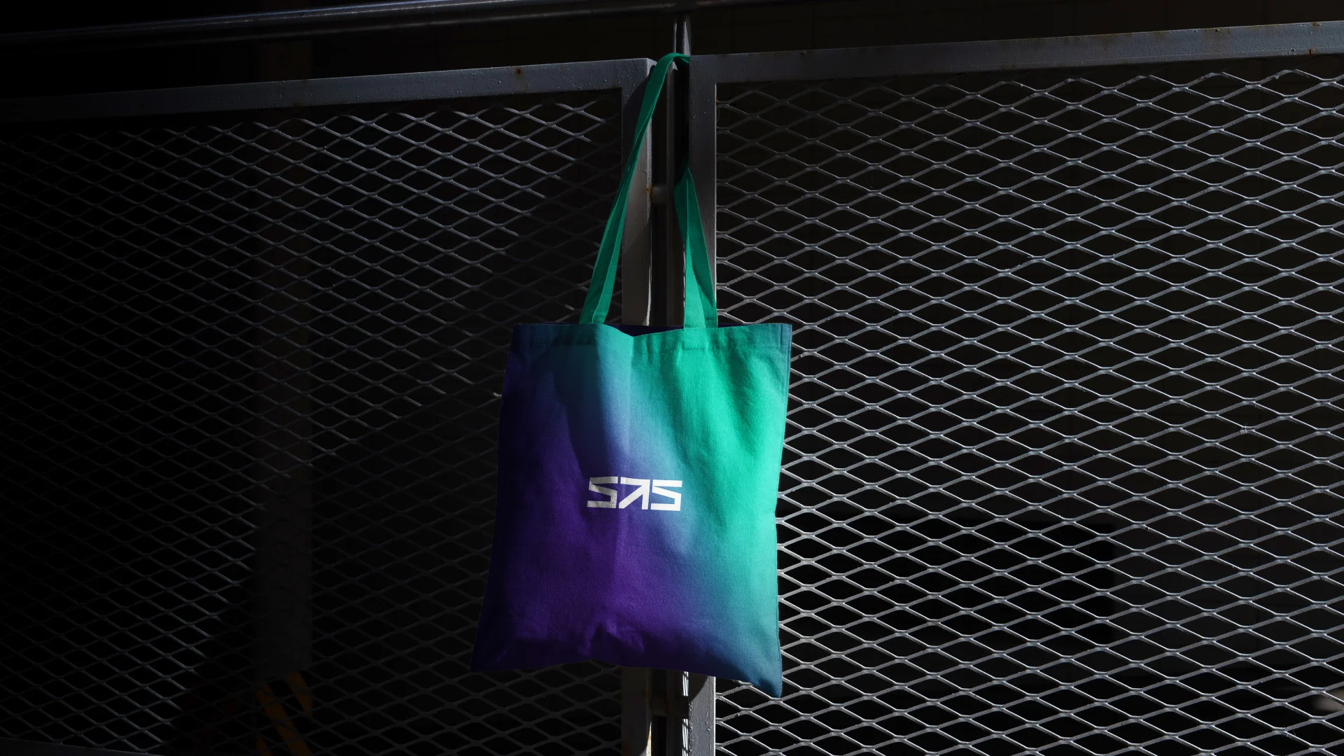 Projeto SAS Global Financing Solutions da Nhdesign: Tote bag com o gradiente da SAS e o logo a branco no centro pendurada numa grade.