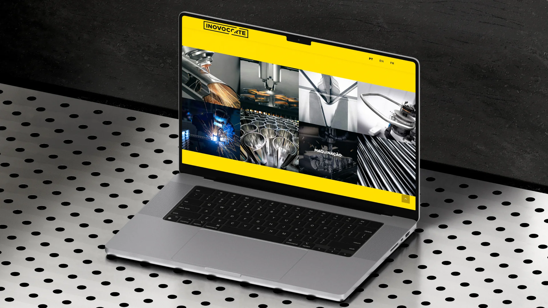 Projeto Inovocorte da Nhdesign: Um portátil sobre uma superfície de metal perfurada exibe imagens de maquinaria industrial no seu ecrã, com um cabeçalho de site amarelo.